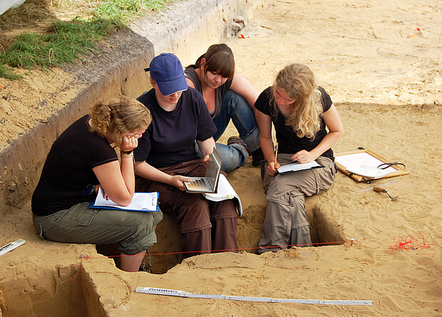 Besprechung auf der Grabung Studentinnen besprechen einen Befund auf der Grabungsfläche